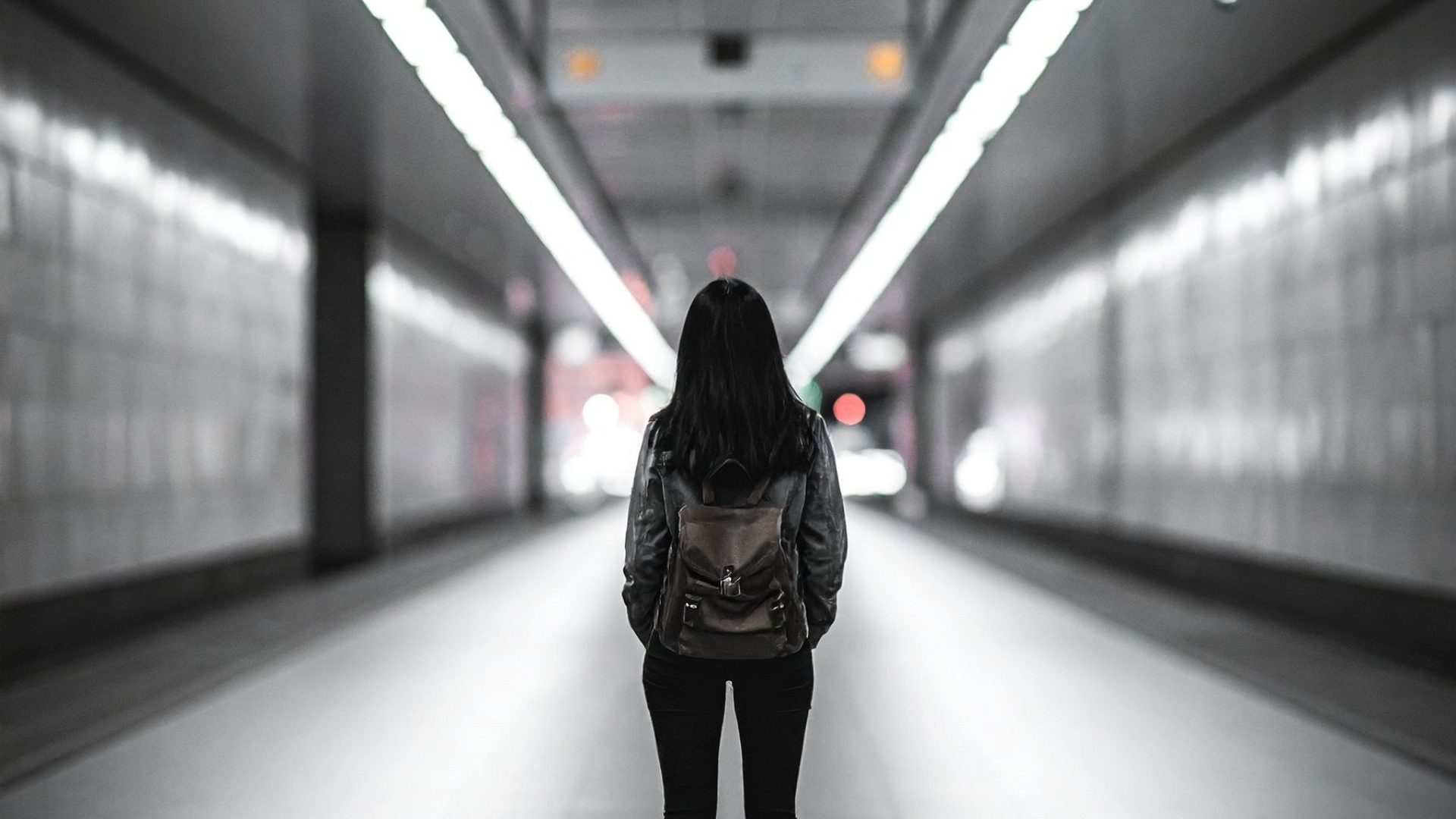 A woman standing at the end of a fluorescent lit hallway. 